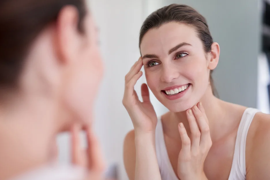 a woman checks her smooth skin in front of the mirror